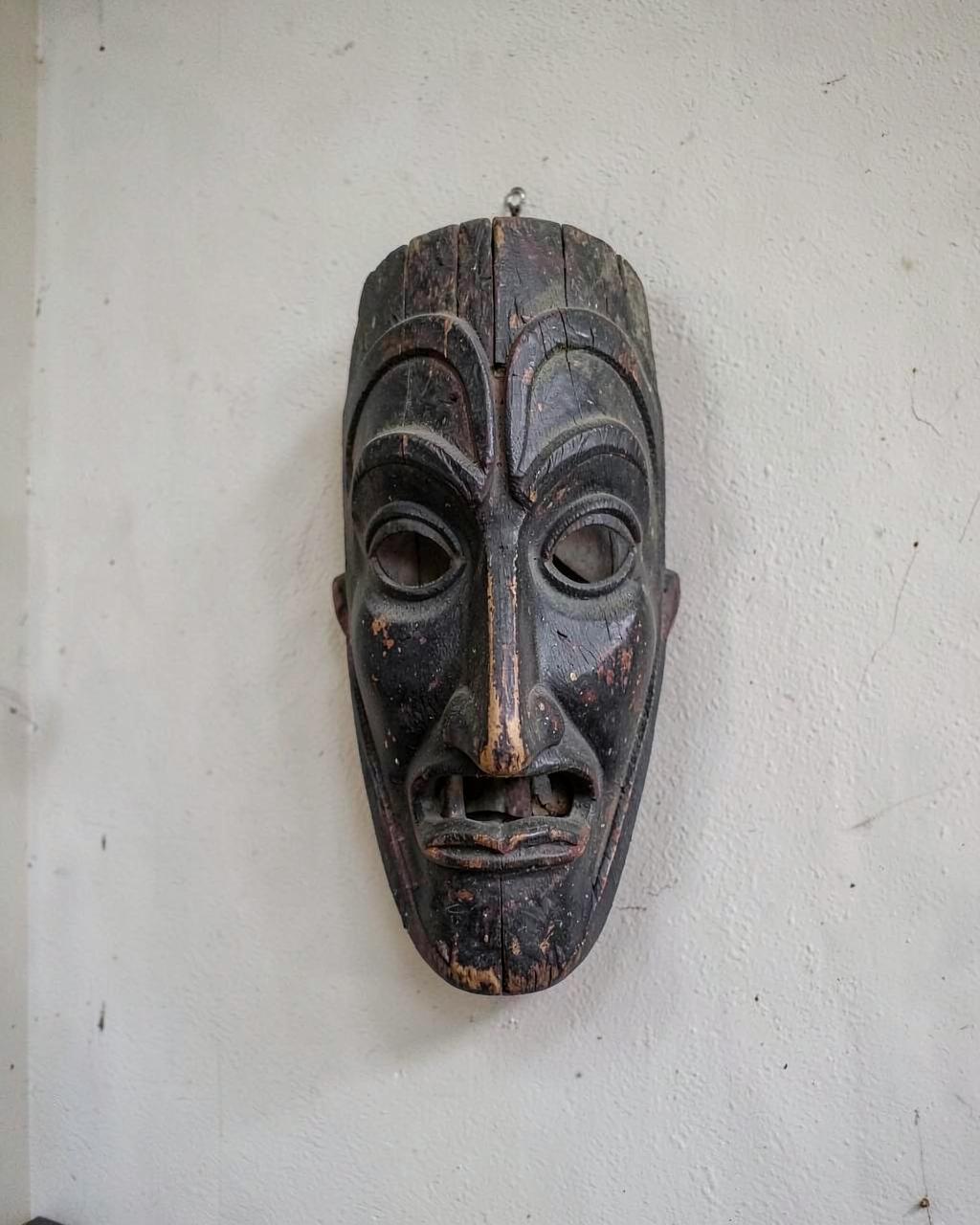 Demo photo: carved wooden mask with dark patina hanging on a pale wall