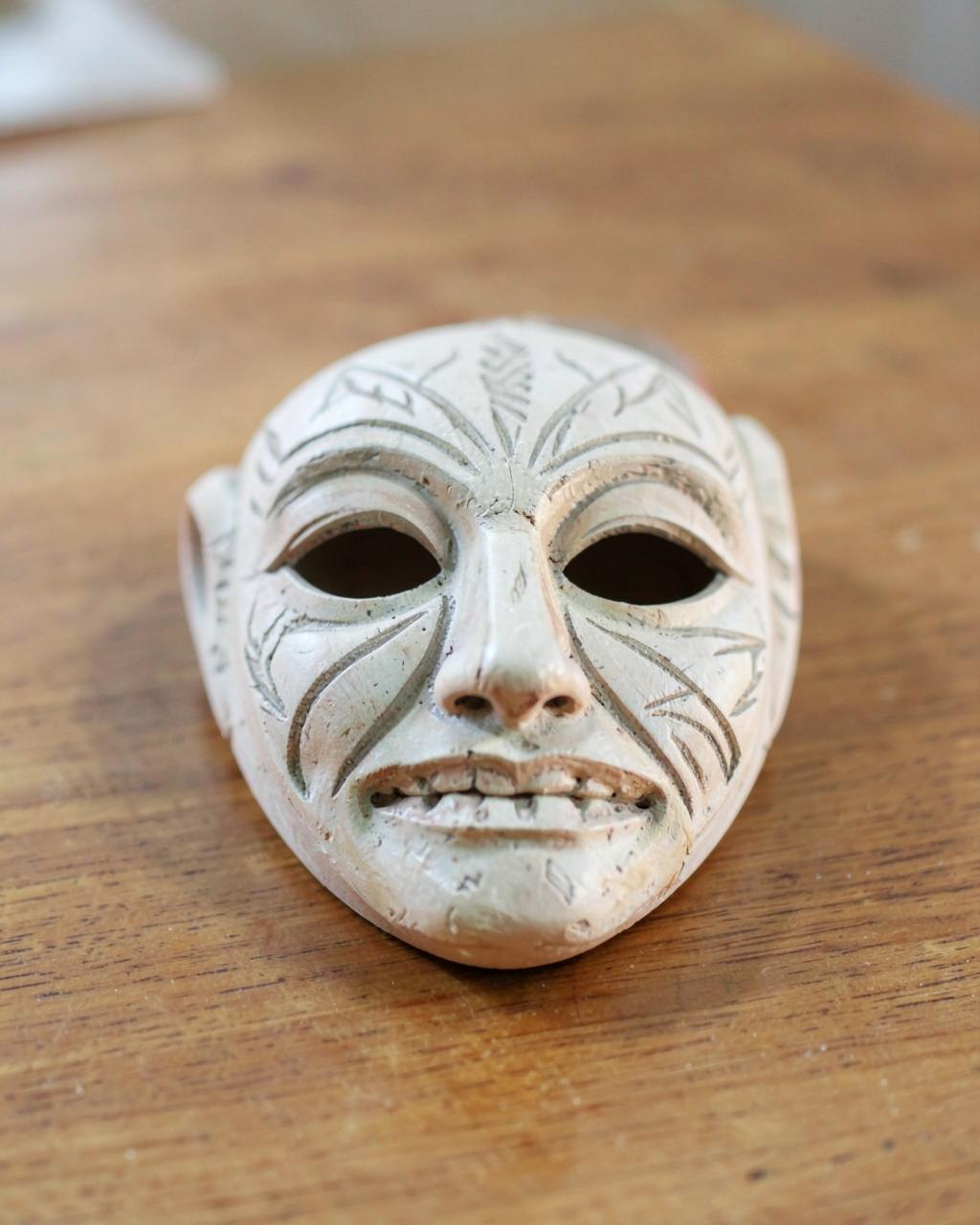 Demo photo: pale painted wooden mask with incised patterns on a wooden table