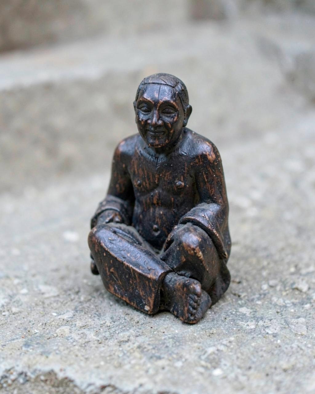 Demo photo: small dark carved wooden seated figure on a stone step
