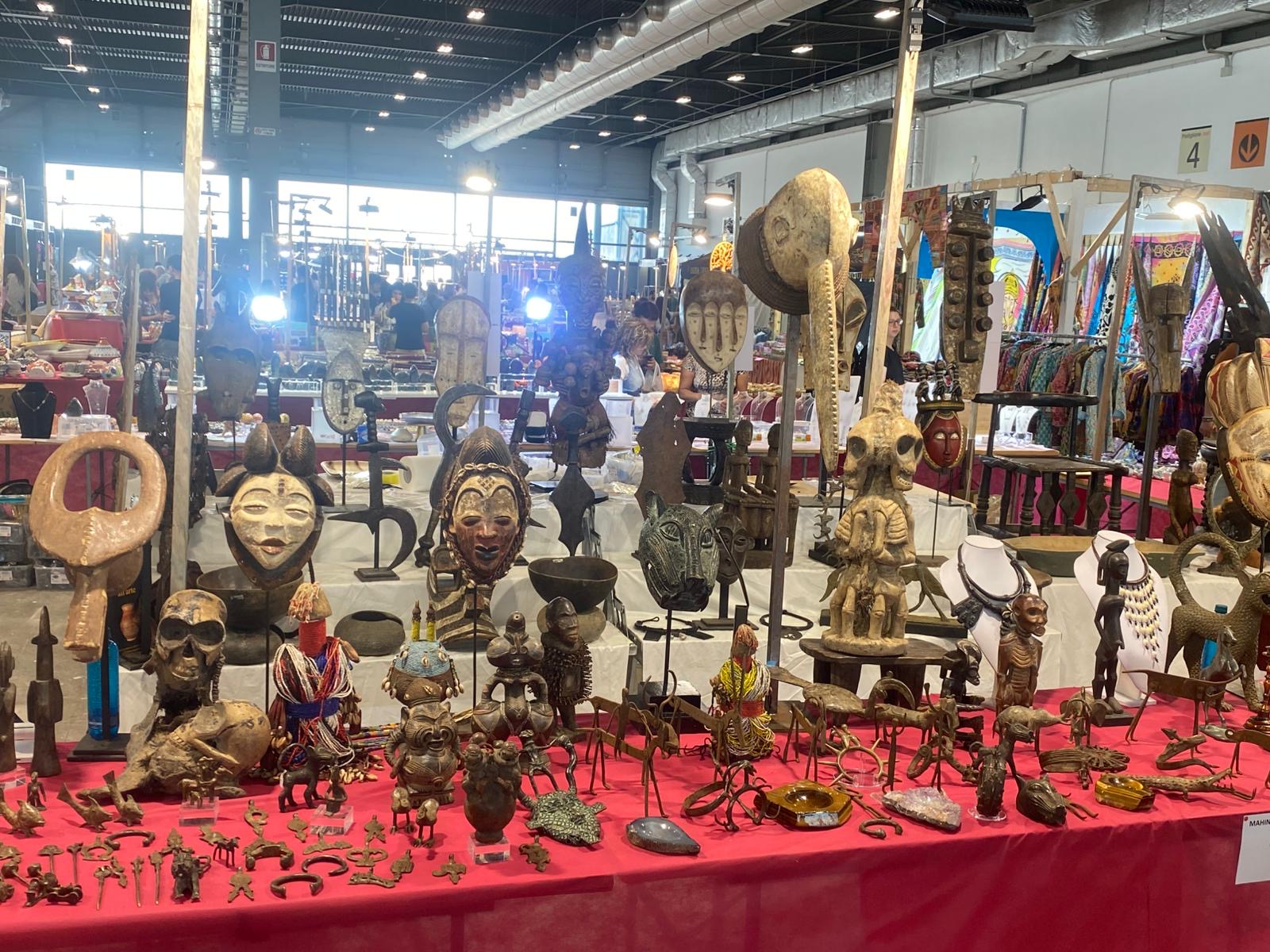 Fair stall with masks, wood figures and small bronzes on a red table